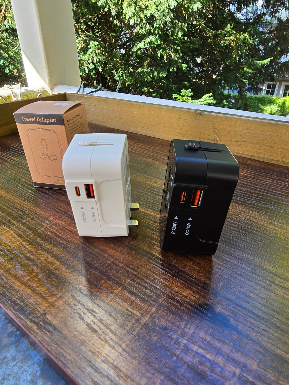 Weißer und schwarzer Universal-Reiseadapter mit Verpackung auf Holztisch.